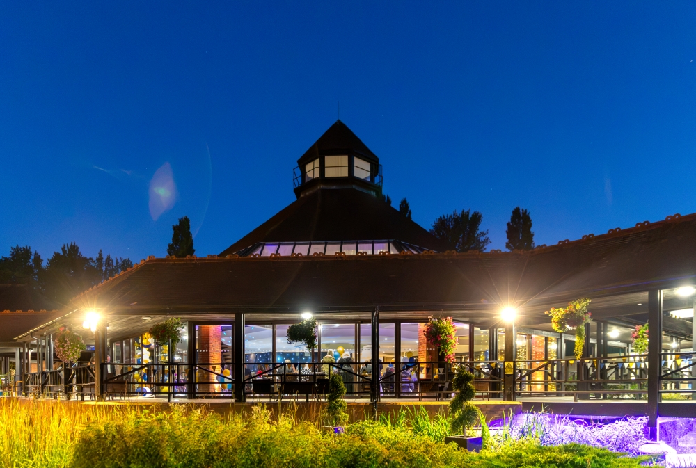 Exterior view of the CIM Business Centre lit up at night showing the illuminated central lantern tower and glass-fronted event space.