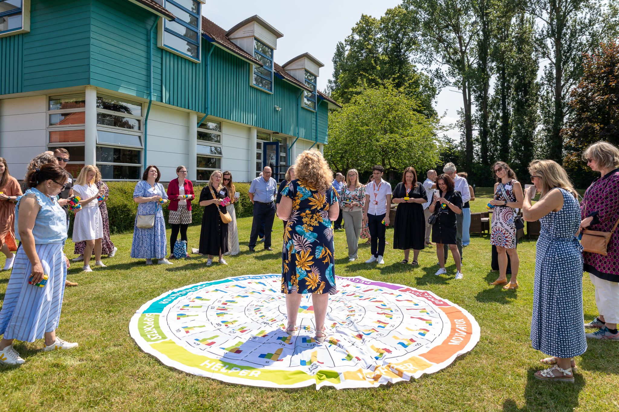 Delegates standing in a circle outdoors around an interactive learning mat on the lawn at CIM Business Centre.